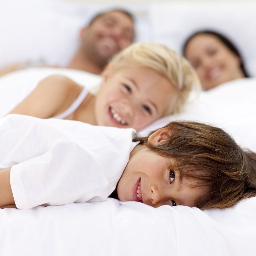 famiglia vestita di bianco nel lettone con bambino in primo piano